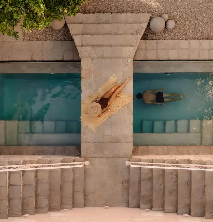 Minimalist stone architecture featuring a view of a person swimming in the turquoise pool at La Valise San Miguel Hotel.
