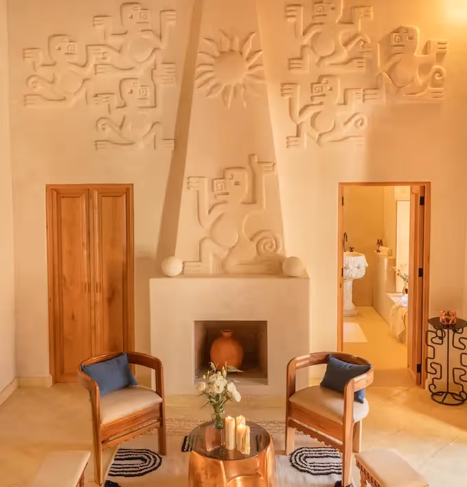 Elegant lounge featuring a modern fireplace, wooden armchairs, and an artistic relief wall at La Valise San Miguel Hotel.