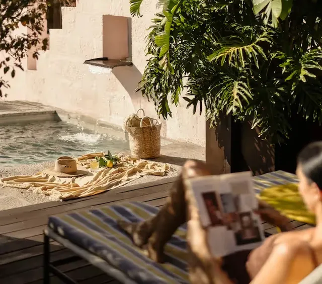 Guest reading on a lounger beside the pool fountain and tropical plants at La Valise San Miguel de Allende