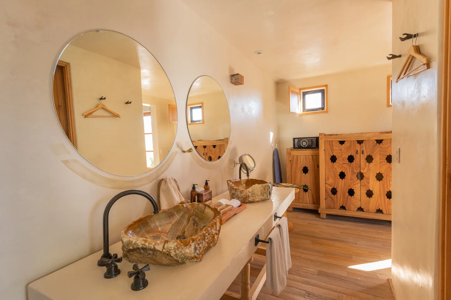 Tocador de la Aura Suite con lavabo de madera petrificada, espejos redondos y armario tallado — La Valise San Miguel de Allende
