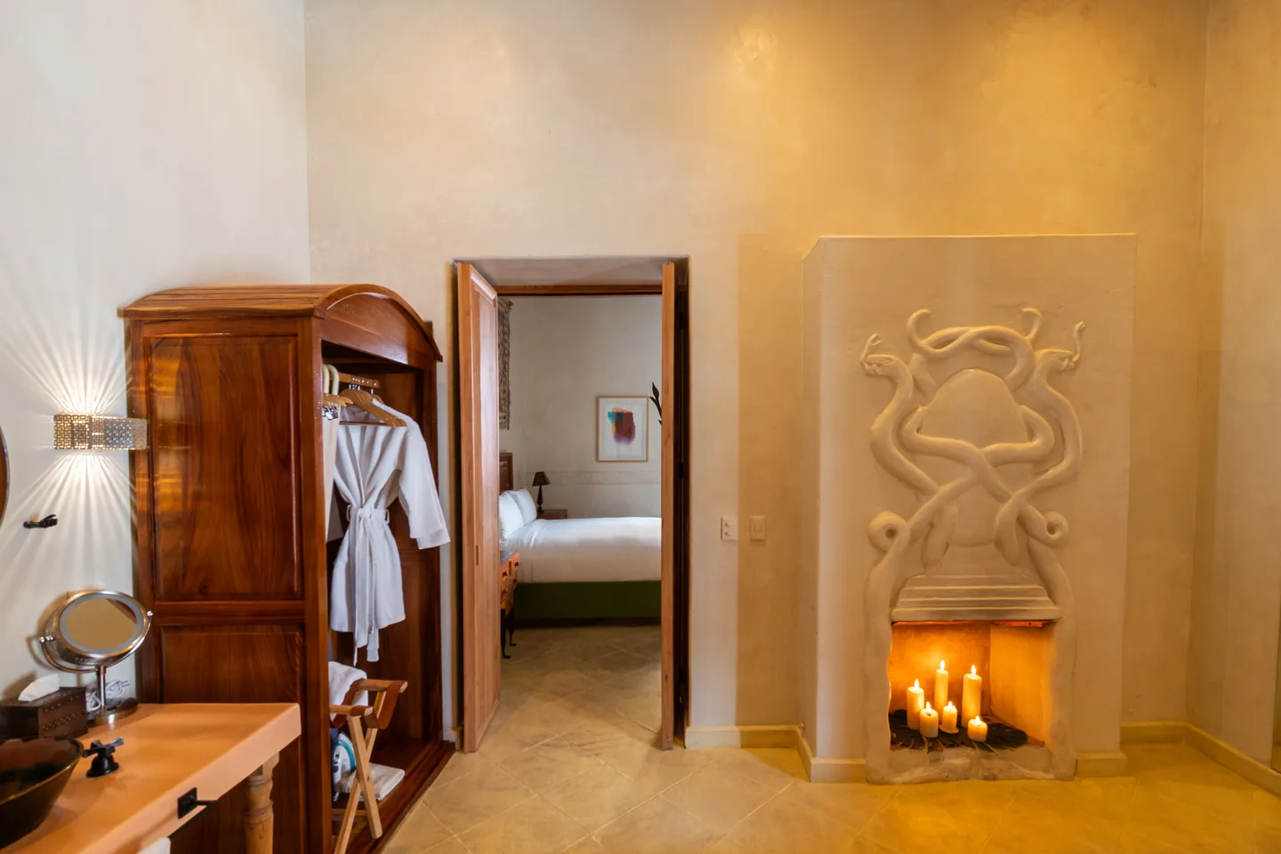 Chimenea iluminada con velas y relieve de serpiente junto al armario en el baño de la Cóatl Suite — La Valise San Miguel de Allende