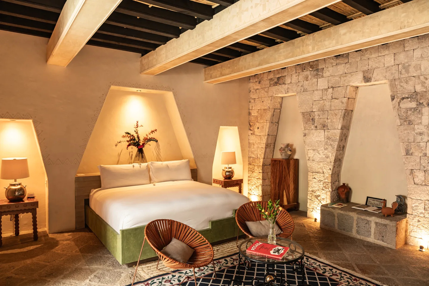 Genesis Suite con cama king en un nicho trapezoidal iluminado, arcos de piedra local y vigas de madera pesada — La Valise San Miguel de Allende