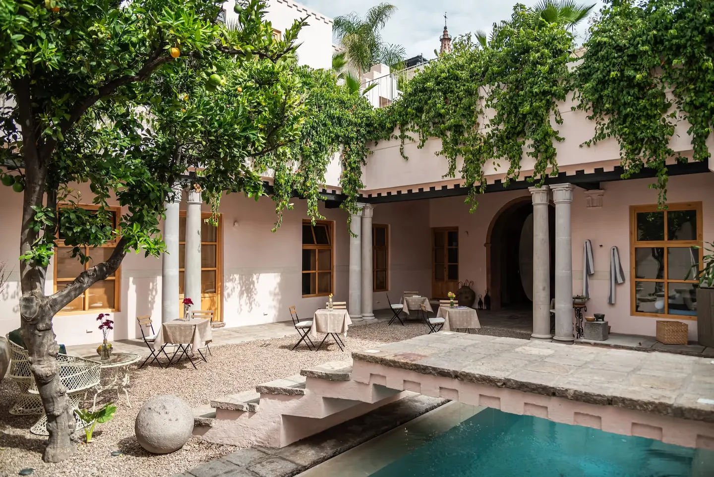 Colonial courtyard with stone columns, climbing vines, loungers and the pool at La Valise San Miguel de Allende