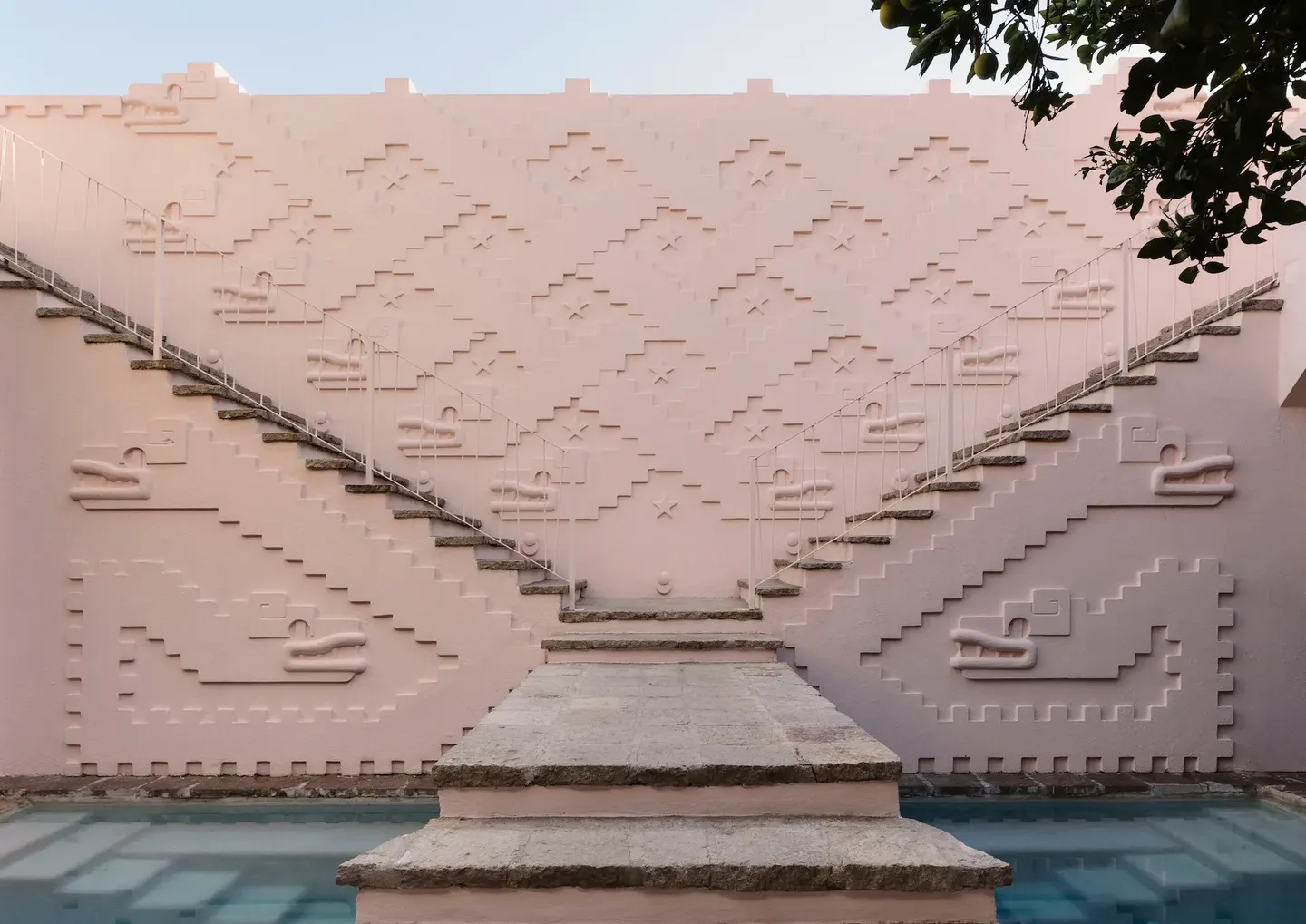 Symmetrical pink staircases with geometric reliefs leading up from a reflective pool at La Valise San Miguel de Allende